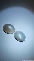 Pair of natural oval cabochon moonstones shown on white background, highlighting smooth surface and reflective sheen characteristic of moonstone.