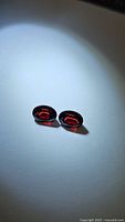 Top view of two oval faceted cherry red garnet gemstones under bright light on white background highlighting their clarity and color.