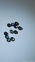 Ten small round cut multicolored sapphires scattered on a white background showing various shades of blue, green, and purple.
