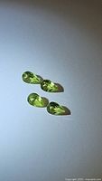 Four pear cut apple green peridot gemstones arranged on a white background showing size, shape, and color.