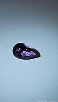 Pear cut natural purple amethyst gemstone photographed on a neutral background highlighting color and faceting.