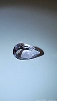 Clear photo of a pear-shaped light purple-pink amethyst gemstone on a plain surface with light reflection.