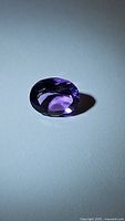 Close-up photo of a single natural purple amethyst gemstone, oval cut, showing deep purple color and clarity.