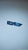 Two rectangular baguette cut deep blue Swiss blue topaz gemstones side by side on a plain surface.