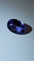 Close-up photo of the deep blue oval cut Tanzanite gemstone on a neutral surface showing facets and color.