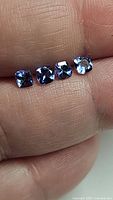 Four cushion cut tanzanite gemstones held on a finger, showing their size and color in natural light.