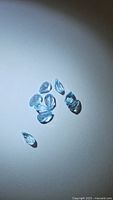 Nine pear cut sky blue topaz gemstones laid out on a white or light surface illuminated to show the clarity and blue color.