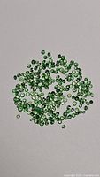 Diamond cut natural green tsavorite garnet gemstones spread out on a white background, showing multiple small round stones.