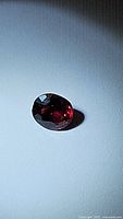 Oval faceted natural ruby with intense blood red color, photographed on a plain surface under light to show color and clarity.