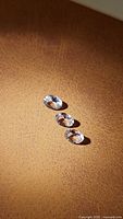 Three oval cut natural untreated morganite gemstones displayed on a textured tan surface under warm lighting, showing their clarity and color.