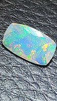 Close-up photo of the natural Ethiopian opal showing intense multicolored flash on a black textured background.