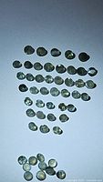 Photo of multiple small round faceted alexandrite gemstones in green hue under neutral light showing size and shape.