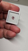 Hand holding white display box with oval pink sapphire centered on foam insert