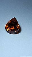 Pear-shaped spessartite garnet gemstone displaying its vibrant orange color and faceted cut.