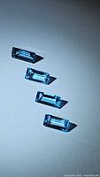 Overhead photo of four rectangular baguette cut natural Swiss blue topaz gemstones arranged vertically on a light background.