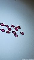 Multiple small oval cut natural rubies laid out on a white surface showing deep reddish-pink color and clarity.
