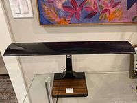 Front view of lamp showing black rectangular shade, pedestal, wood veneer base