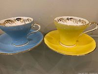 Yellow and blue Aynsley teacups with saucers side by side