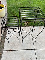 Two black wrought iron plant stands side by side on patio