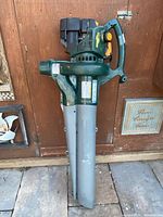 Full view of Yardworks gas leaf blower with grey dual tubes against door