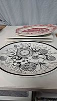 Two rectangular white serving platters stacked, with black and white floral design oval platter in front