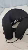 Front view of black fabric neck massager with attached power cord