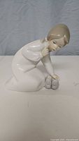 Porcelain figurine showing child figure examining slippers from side view.