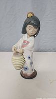 Front view of the Lladró porcelain figurine showing the Japanese girl holding a lantern in front, wearing a kimono with blue flowers.
