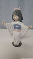 Front view of the Lladro figurine showing the girl with a pink bow holding a flower, dressed in white kimono with blue and pink details.