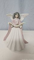 Front view of the porcelain angel figurine dressed in a pink cloak with white wings holding a scroll.