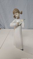 Front view of the porcelain figurine depicting a girl holding a mandolin in a white dress with brown hair in pigtails.