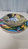 Stack of round porcelain plates with colorful artistic designs including ballerina and ribbon patterns