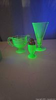 Three pieces of green uranium glassware set shown under UV light, fluorescing bright green