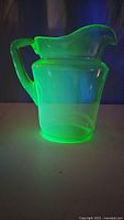 Uranium glass pitcher glowing bright green under UV light, showing the characteristic uranium glass fluorescence.