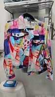 Front view of the jacket hanging on a hanger showing the full multicolor abstract print and button closure.