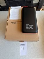 Power bank with box and instruction booklet, black carbon fiber textured finish.