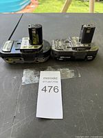 Photo showing both Ryobi 18V batteries side by side on table with MaxSold lot tag 476.