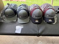 Four Whitaker Richardson 112 caps showing two color variants: gray/black and gray/maroon, all new and some in plastic packaging.