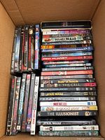 Photo of large assortment of DVD cases stacked in a cardboard box showing titles from various genres.