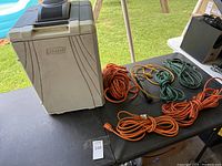 Table setup showing Coleman cooler and multiple extension cords in orange, green, and yellow, plus one power strip extension cord.