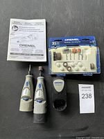 Two Dremel rotary tools, a charger, instruction booklet, and a 31-piece accessory kit in a clear plastic case.