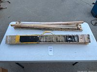 Two adjustable height folding saw horses folded flat on a table, one with yellow and black paint on crossbar, showing condition and design.