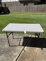 Full view of white folding table on a concrete surface with grass in background.