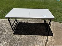 Full view of white folding table set up outdoors on concrete with grassy background