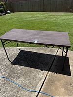 Full view of the brown folding table set up outdoors on concrete with grass background.