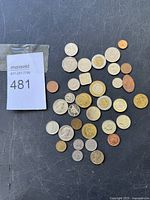 A mixed collection of about 40 foreign coins in different shapes and sizes, laid out on a surface with a MaxSold tag present.
