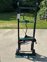 Front view of green Harper appliance dolly standing upright outdoors on concrete with securing strap visible.