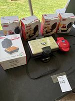 Photo of five Dash kitchen mini appliances with boxes and two unboxed units on a table outdoors.