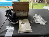 Full view of the hand mixer with power cord, two wire whisk attachments, instruction manual, and original box on a black table outdoors.