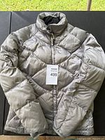 Full view of gray puffer jacket laid flat, showing the front side with collar and full zipper.